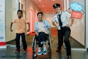 Tai Young sitting in a wheelchair, next to a police woman and a young boy. They are standing in a hall, posing for the camera.