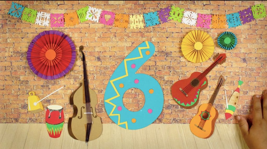 A brick wall design that has a Mexico theme with musical instruments and brightly coloured paper ornaments. There is a large ornamental blue number six in the middle of the wall.